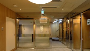 Un pasillo moderno de hotel con puertas de vidrio, una escalera y una señal de salida visible.