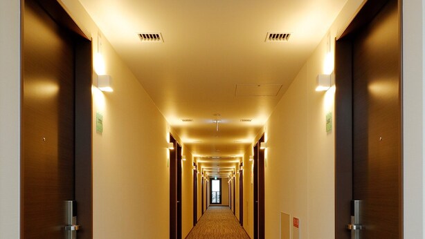 Un pasillo de hotel con pisos alfombrados, puertas de madera e iluminación en el techo.