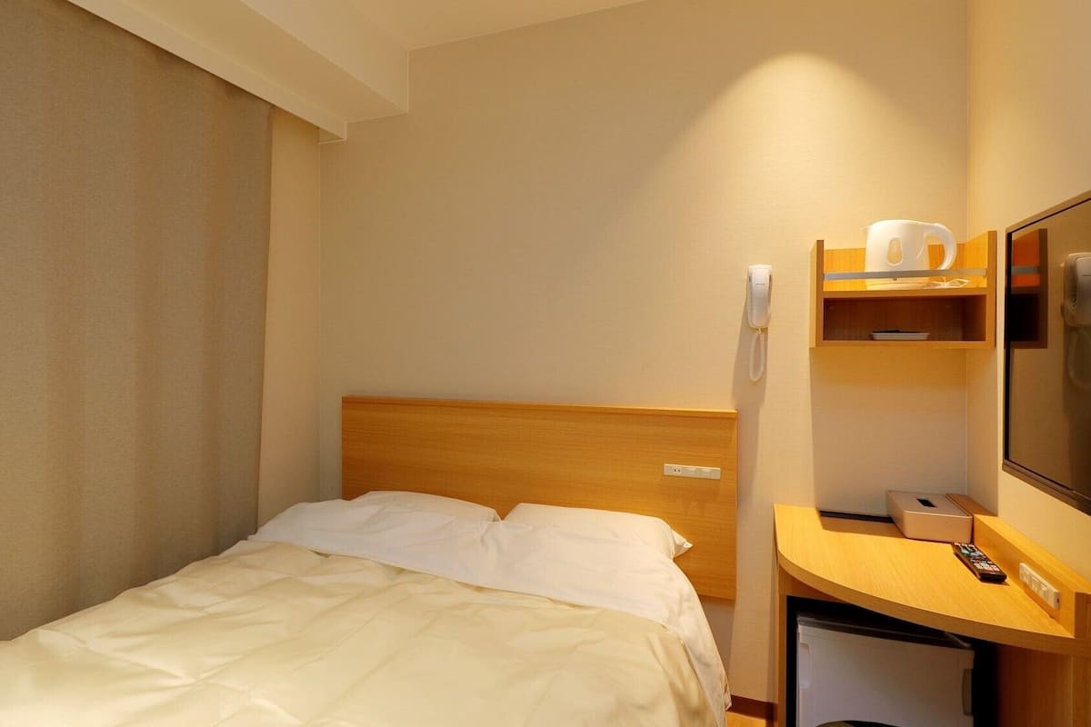 A hotel room with a bed, a wooden desk, a telephone, and a television.
