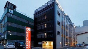 Un edificio de varios pisos con entrada a un estacionamiento, un letrero que indica zona de estacionamiento las 24 horas y una entrada visible al edificio.