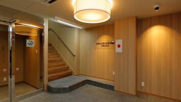 A hotel lobby with a wooden staircase, a sign indicating a hotel lounge, and a security camera on the wall.
