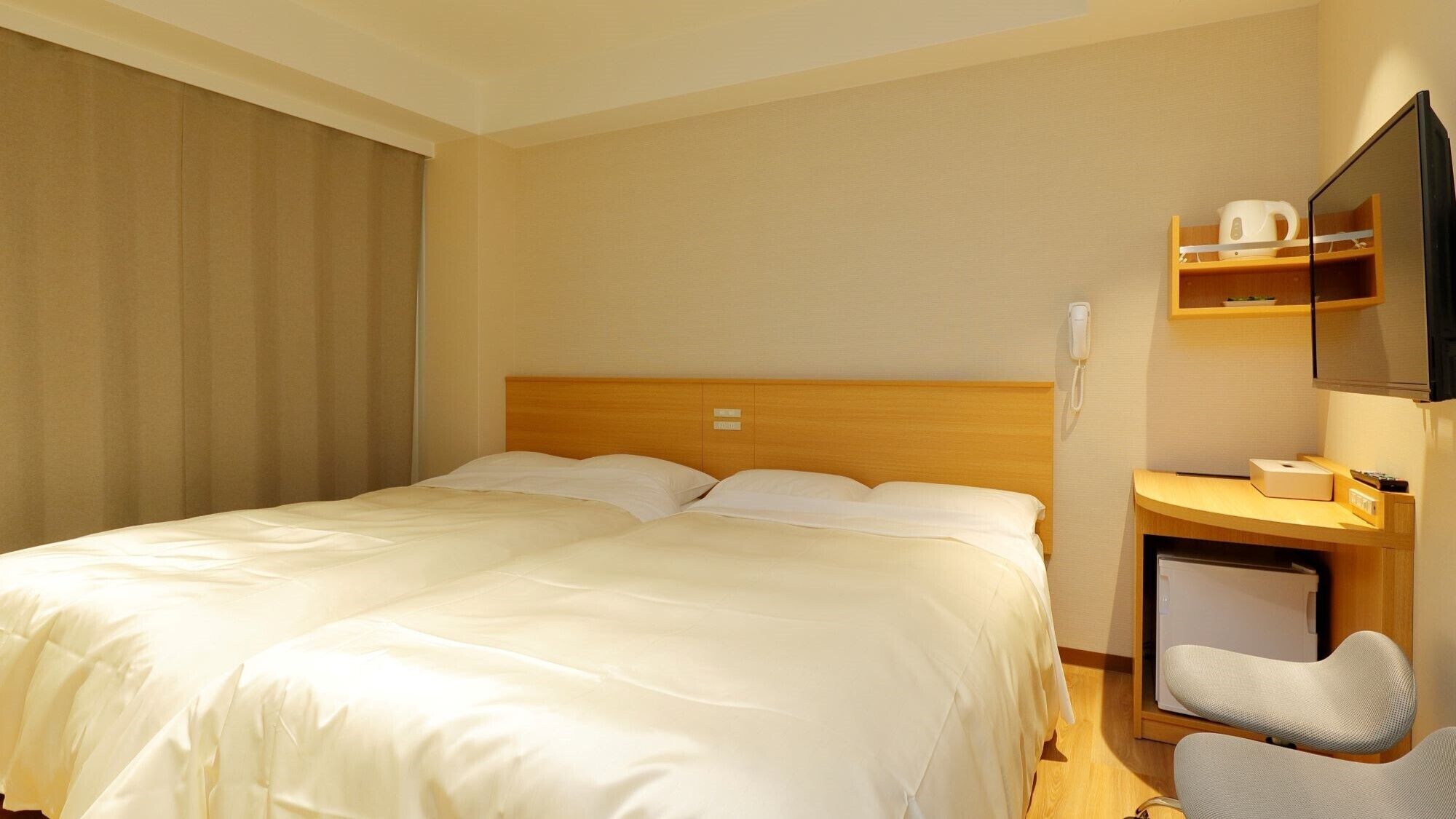 Een hotelkamer met een bed, een bureau met stoel, een telefoon en een televisie.