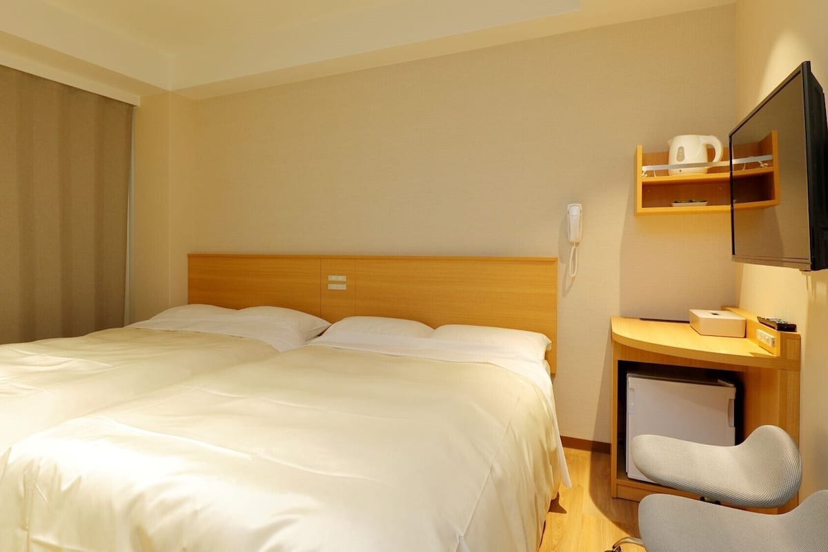 A hotel room with a bed, a desk with a chair, a telephone, and a television.