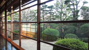 A traditional Japanese-style room with tatami flooring and a view of a well-maintained garden with various trees and shrubs. - Kogushiya (Shimonoseki)
