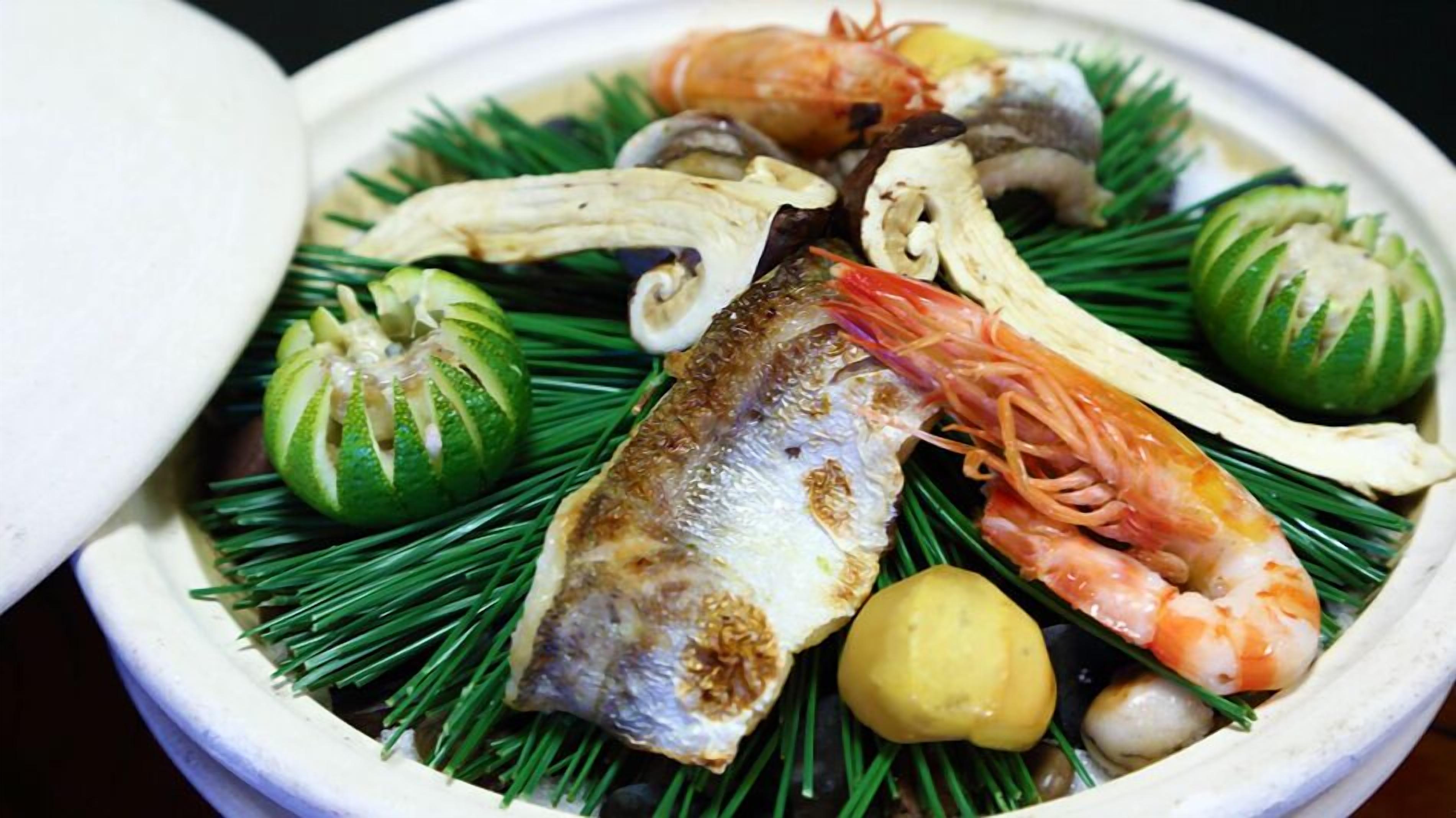 A bowl of seafood with shrimp, fish, and mushrooms on a bed of green leaves.