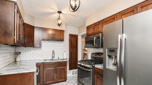 A kitchen with wooden cabinets, a stainless steel refrigerator, a built-in oven, a microwave, and a patterned tile floor.