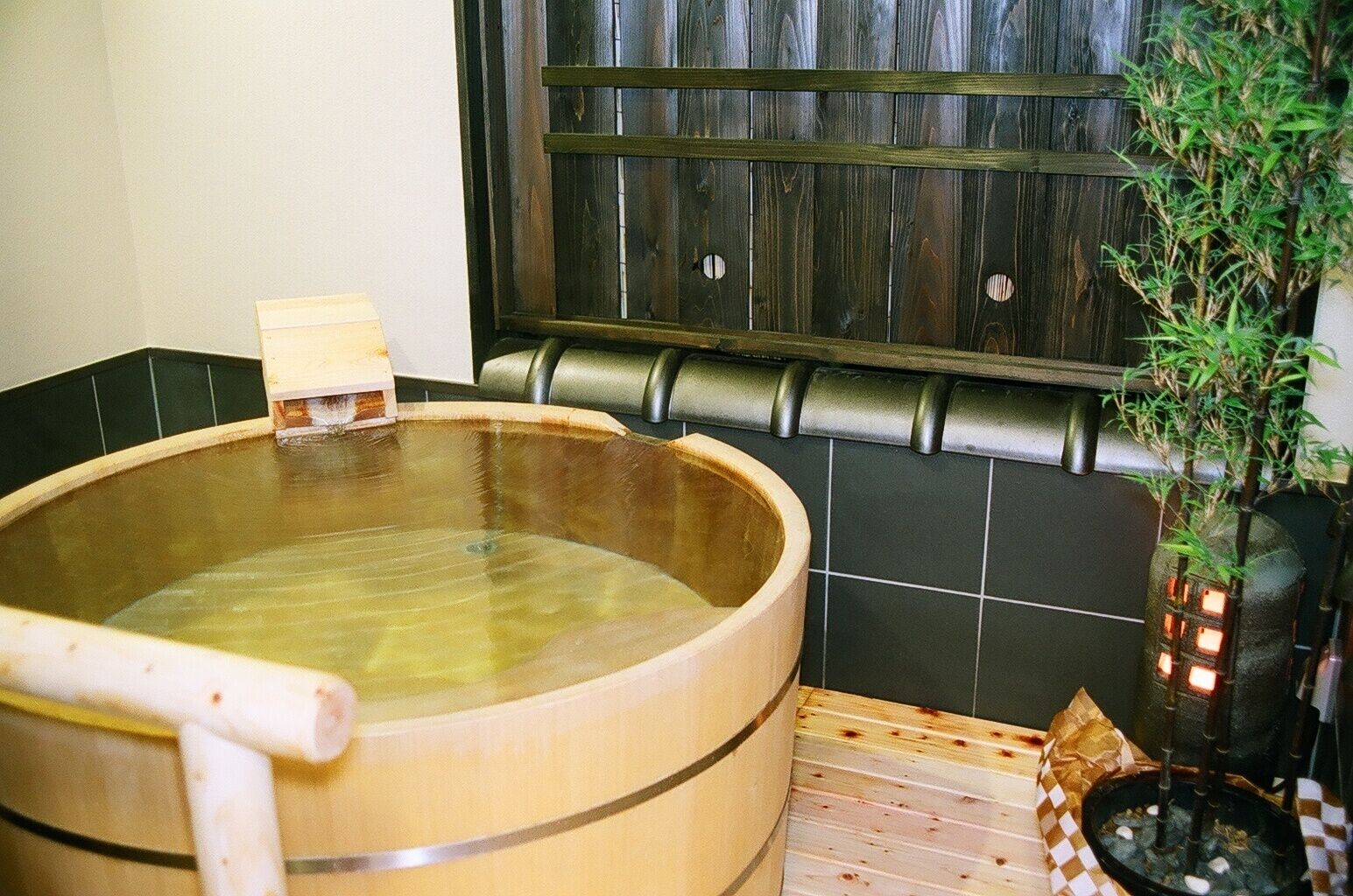 A wooden hot tub with a wooden bench, a small wooden stool, and a potted plant.