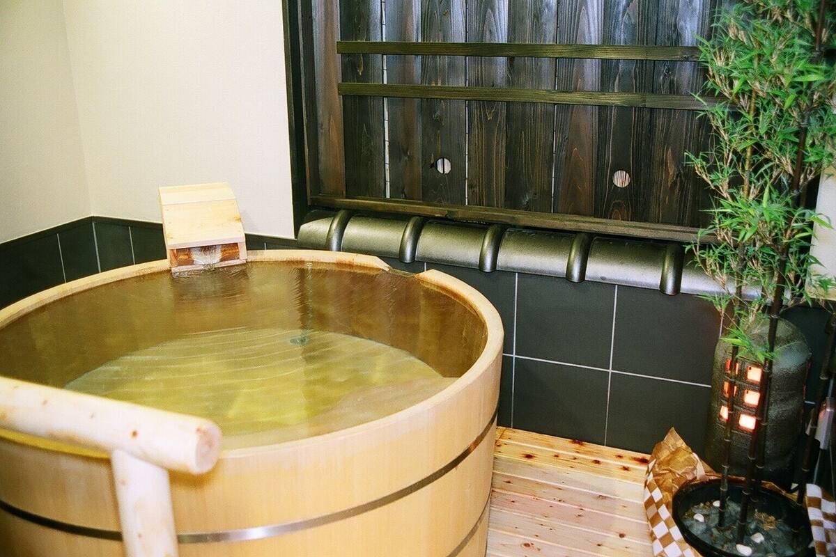 Uma banheira de hidromassagem de madeira com um banco de madeira, um pequeno banquinho de madeira e um vaso com planta.
