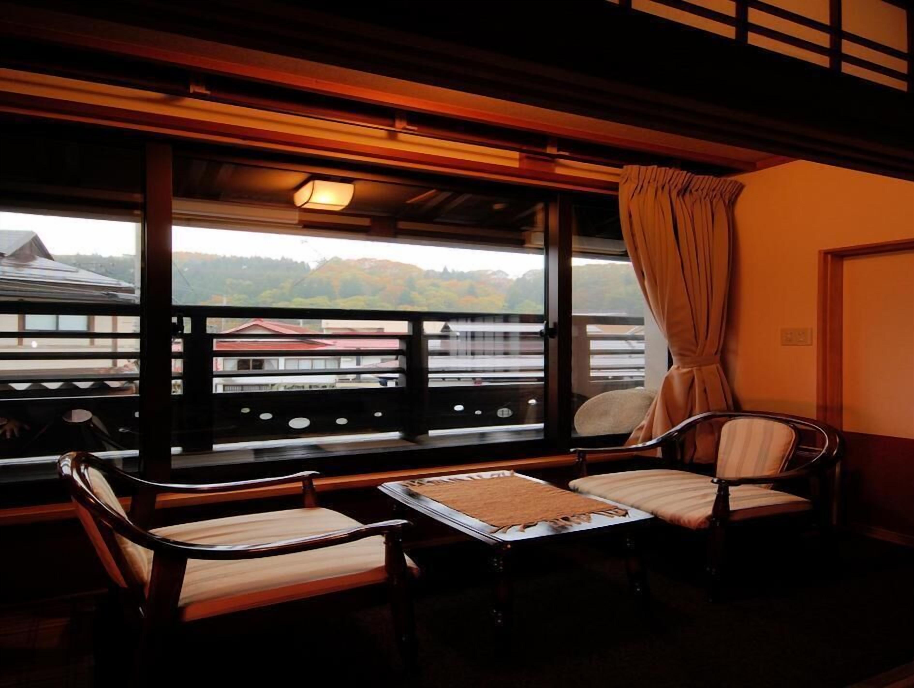 A balcony with wooden furniture, a view of buildings and trees, and a curtain on the window.