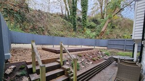 A garden with a wooden staircase leading to a deck, surrounded by a grey fence and a house in the background. -  Holiday rental in Rye, sleeps up to 6 with private gated driveway (Rye)