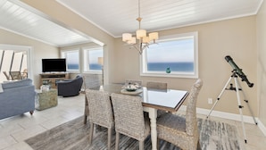 A spacious living room with a dining area, large windows, a television, and a telescope. - Omni Resort - Gorgeous Top Floor Penthouse with Oceanfront Views - Shipwatch! (Fernandina Beach)