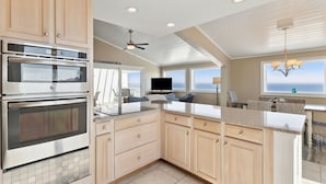 A modern kitchen with built-in ovens, a large island, and a view of the ocean through the windows. - Omni Resort - Gorgeous Top Floor Penthouse with Oceanfront Views - Shipwatch! (Fernandina Beach)