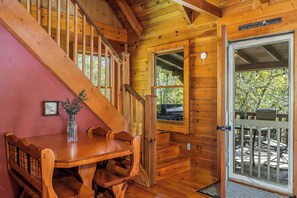 Ein Holzblockhaus-Interieur mit Esstisch, Stühlen, einer Treppe und einer Tür zu einer Außenterrasse.