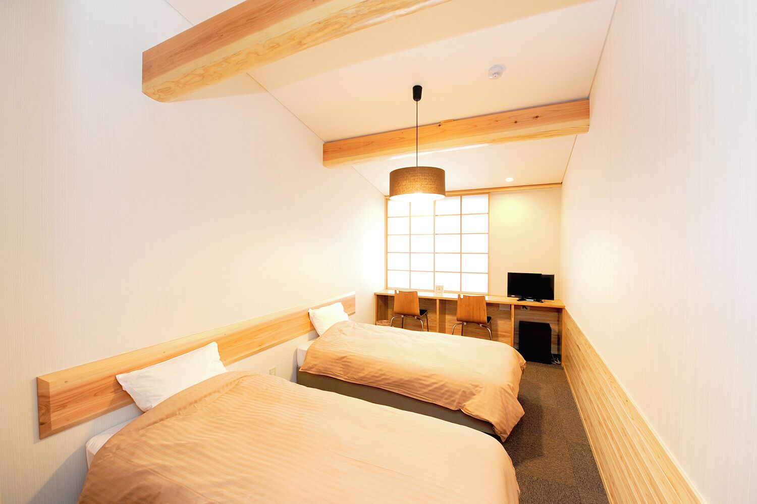 A hotel room with two beds, a TV, and a desk with chairs.