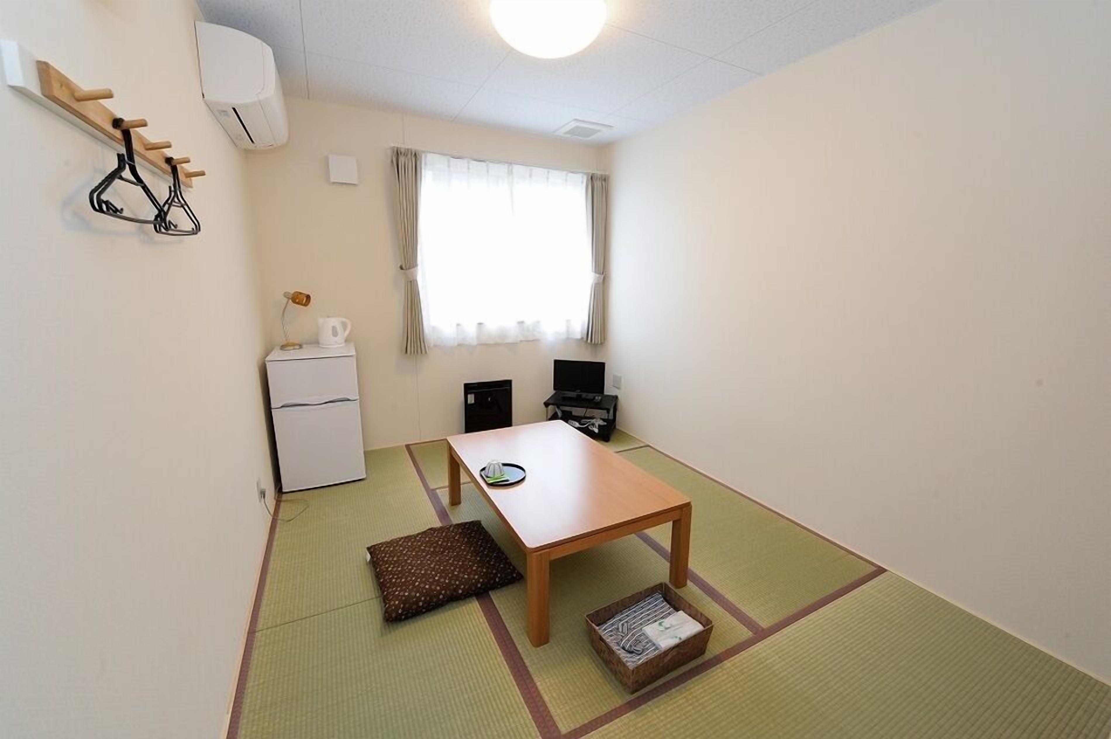 A small room with a wooden table, a white refrigerator, a TV, and a window with curtains.