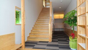 Una escalera de madera con un rellano alfombrado, una planta verde y una estantería de madera.