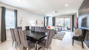 A modern dining room with a large table and grey upholstered chairs, a ceiling fan, and a view through a glass door to an outdoor area. - 1min walk to New Community Pool, Luxury 7BD Home 19016 (Four Corners)