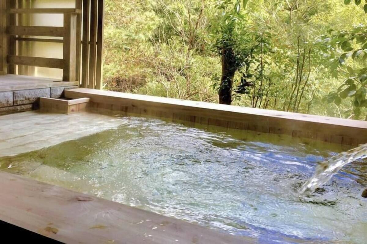 A hot tub with a wooden deck and a view of dense greenery.