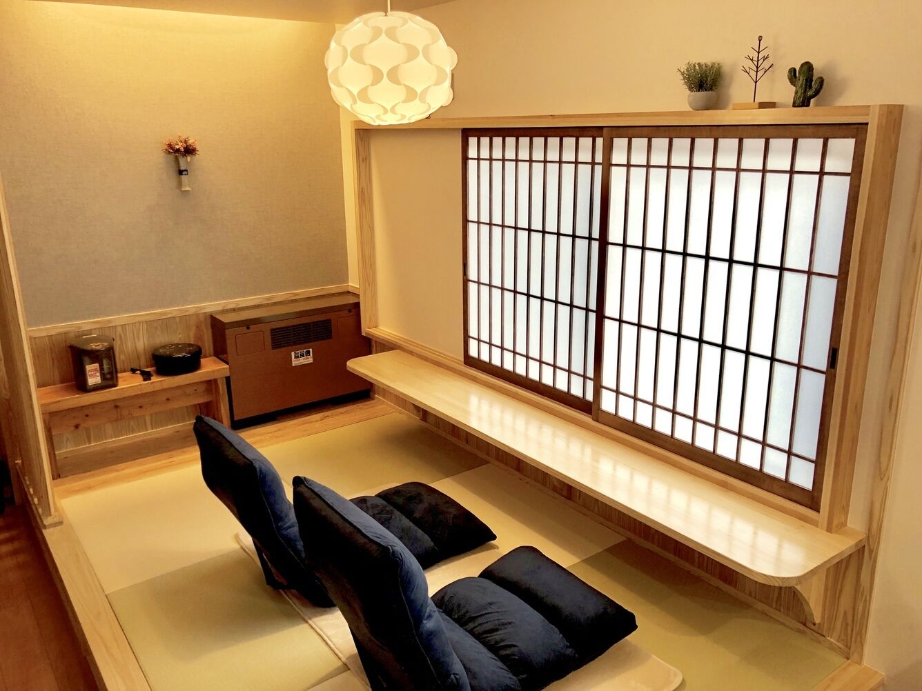 Una habitación con tatami, un shoji, esteras de tatami, una mesa de madera baja y una lámpara japonesa tradicional.