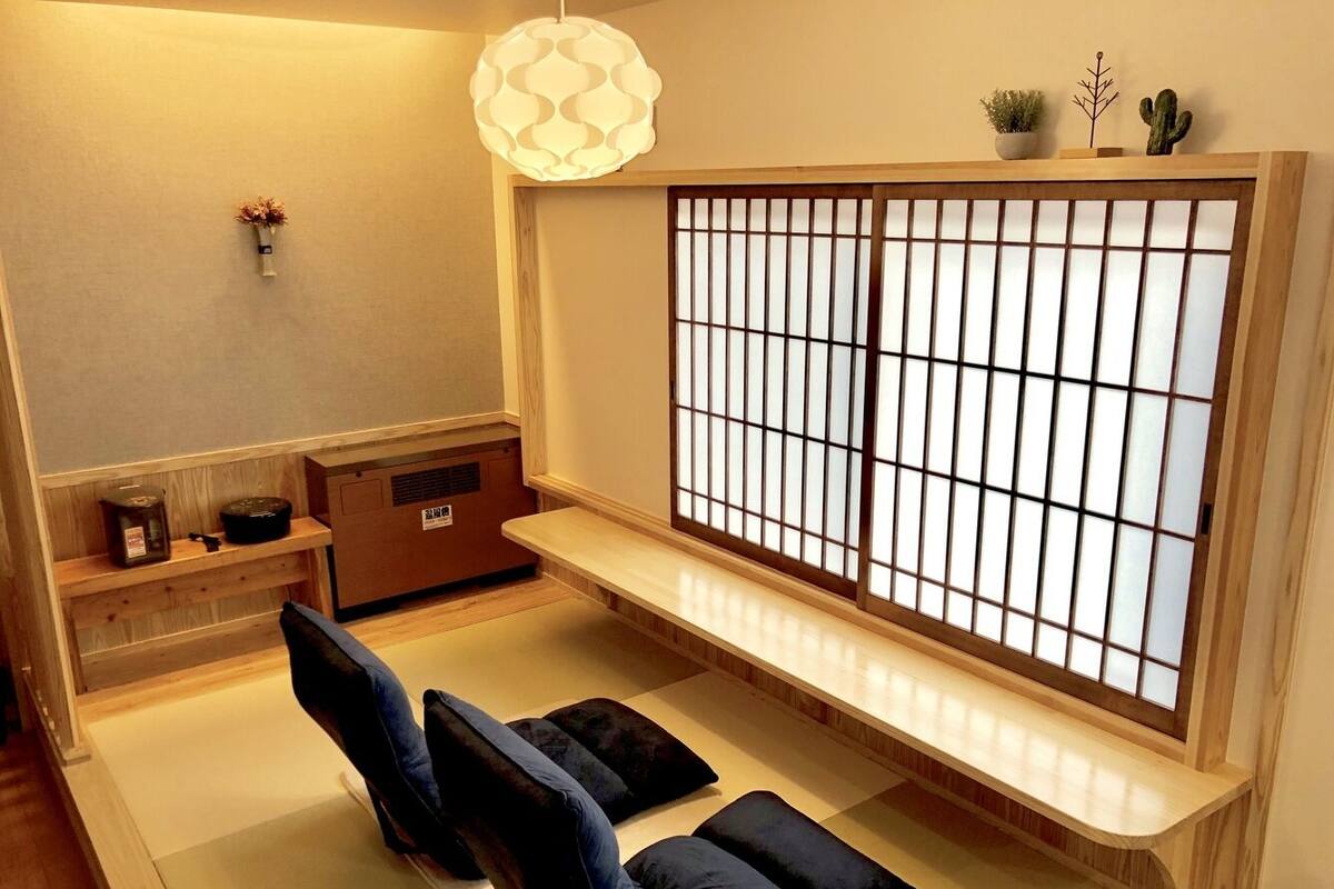 A tatami mat room with a shoji screen, tatami mats, a low wooden table, and a traditional Japanese lamp.