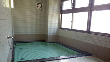 Un baño pequeño con azulejos, zona de ducha, ventana y un enchufe en la pared.