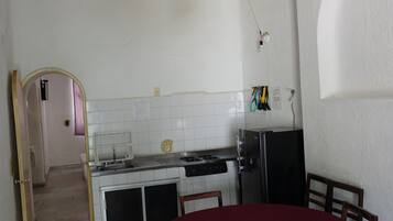 A dining area with a table set for four, a refrigerator, and a kitchen area with a sink and stove.