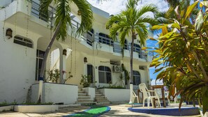 A building with a white exterior, multiple balconies, and a paved courtyard with chairs. - Suites La Audiencia (Manzanillo)