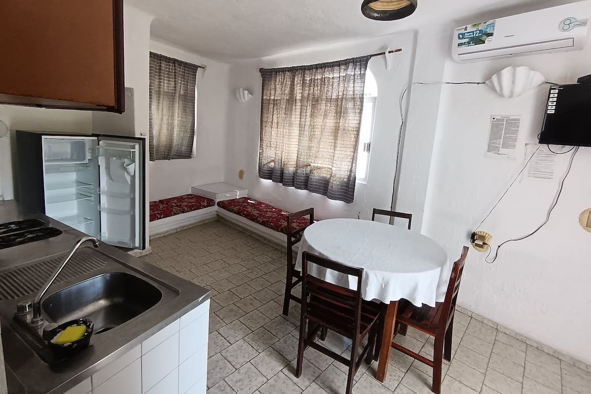 Een kleine keuken met een koelkast, spoelbak en een eethoek met een tafel en stoelen.