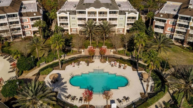 Ein großes Hotel mit einem zentralen Schwimmbecken, mehreren Balkonen und umliegenden Palmen.