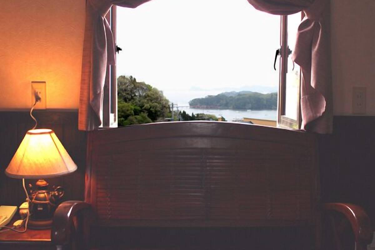 Une chambre avec un lit, une lampe et une vue sur un plan d’eau et des collines.