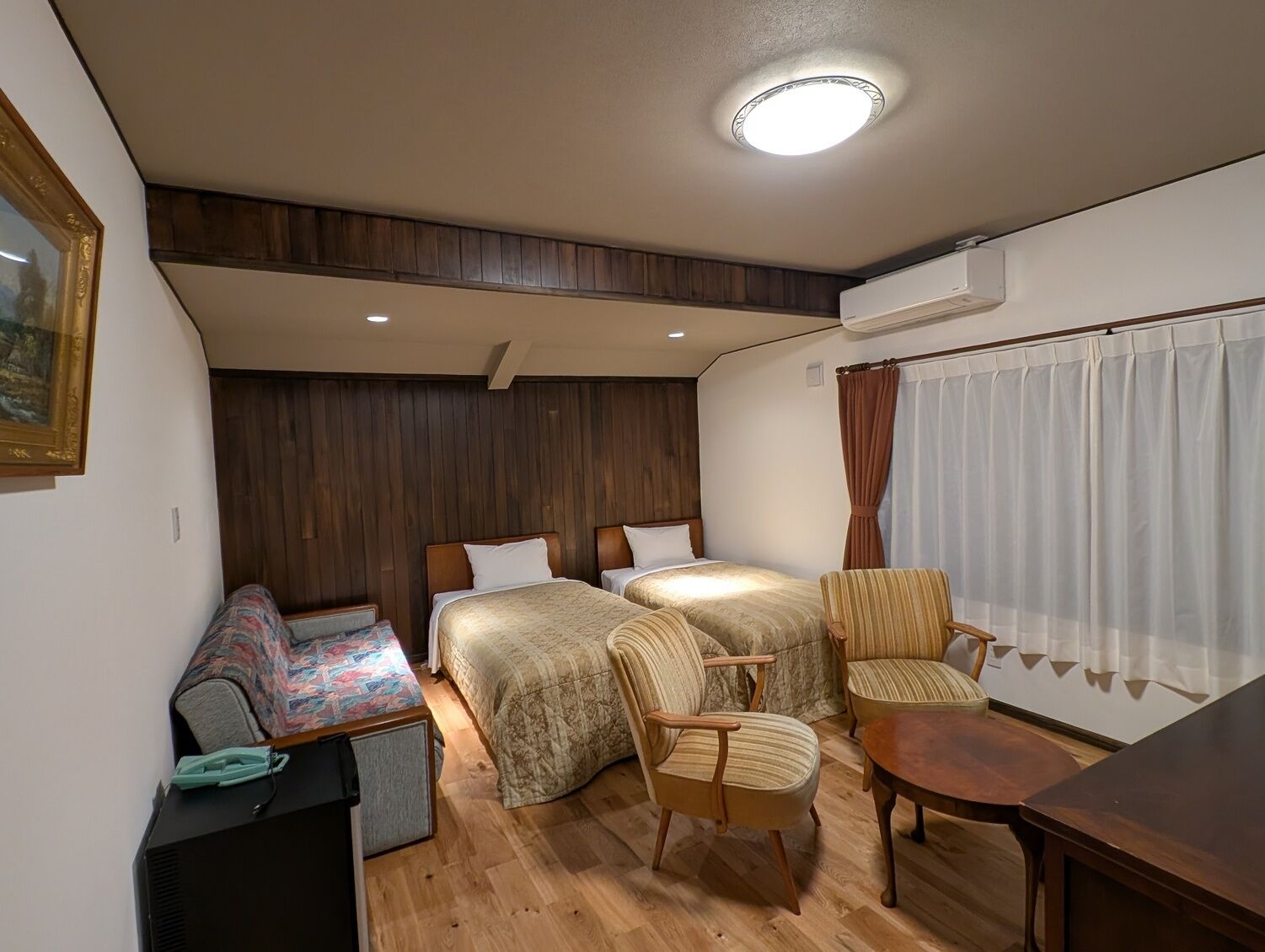 Habitació d'hotel senzilla amb dos llits, un sofà, una taula petita i una cadira.