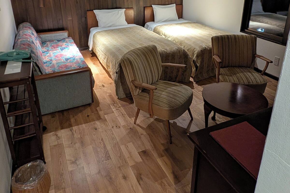 Une chambre d’hôtel de taille modeste, dotée de deux lits, d’un petit coin salon et d’un plancher en bois.