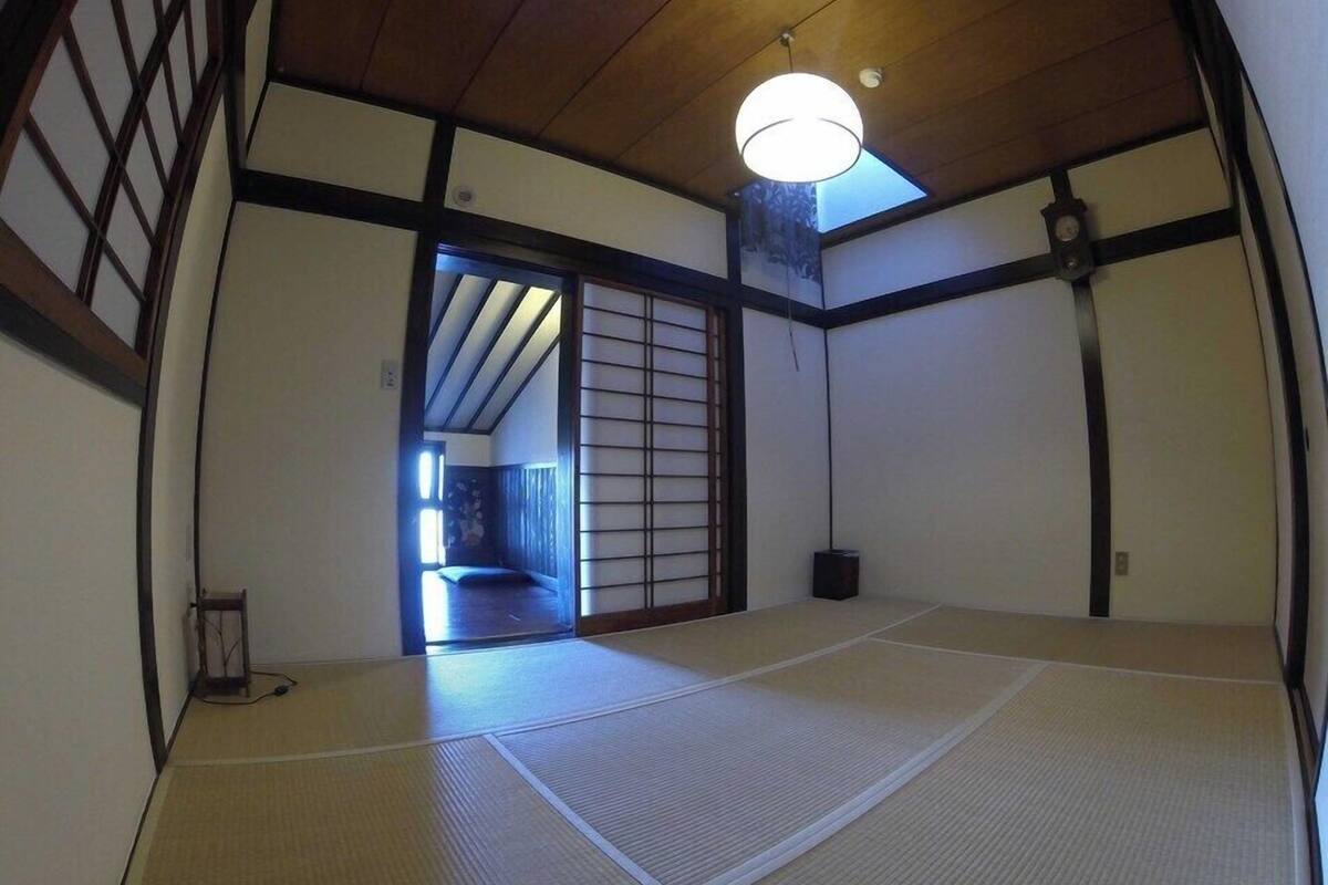 Une pièce de style japonais traditionnel, avec un sol recouvert de tatamis, une porte coulissante en papier de riz (shoji) et un luminaire suspendu.