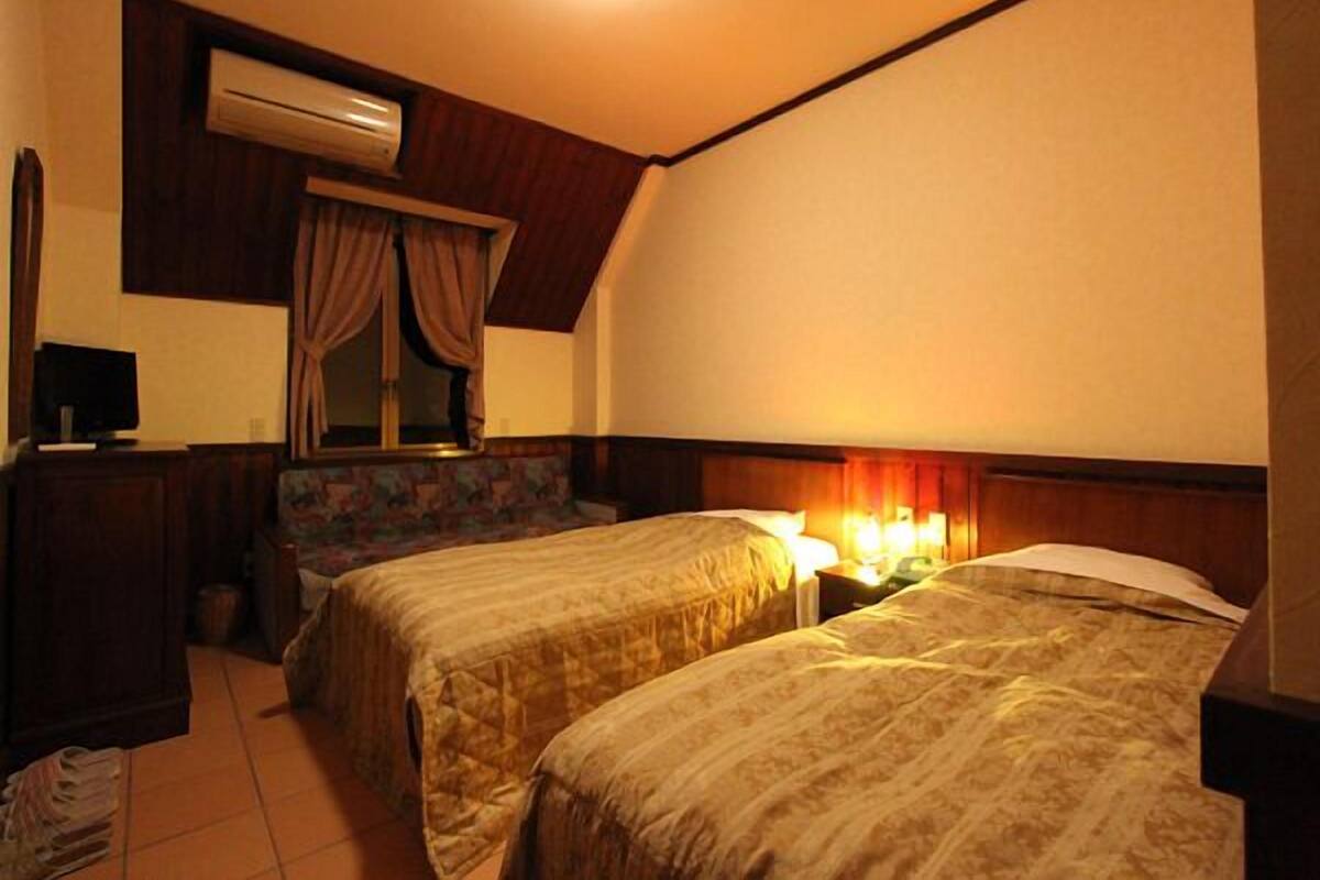 Une chambre d’hôtel avec deux lits, un bureau avec un ordinateur, un appareil de climatisation et une fenêtre avec des rideaux.
