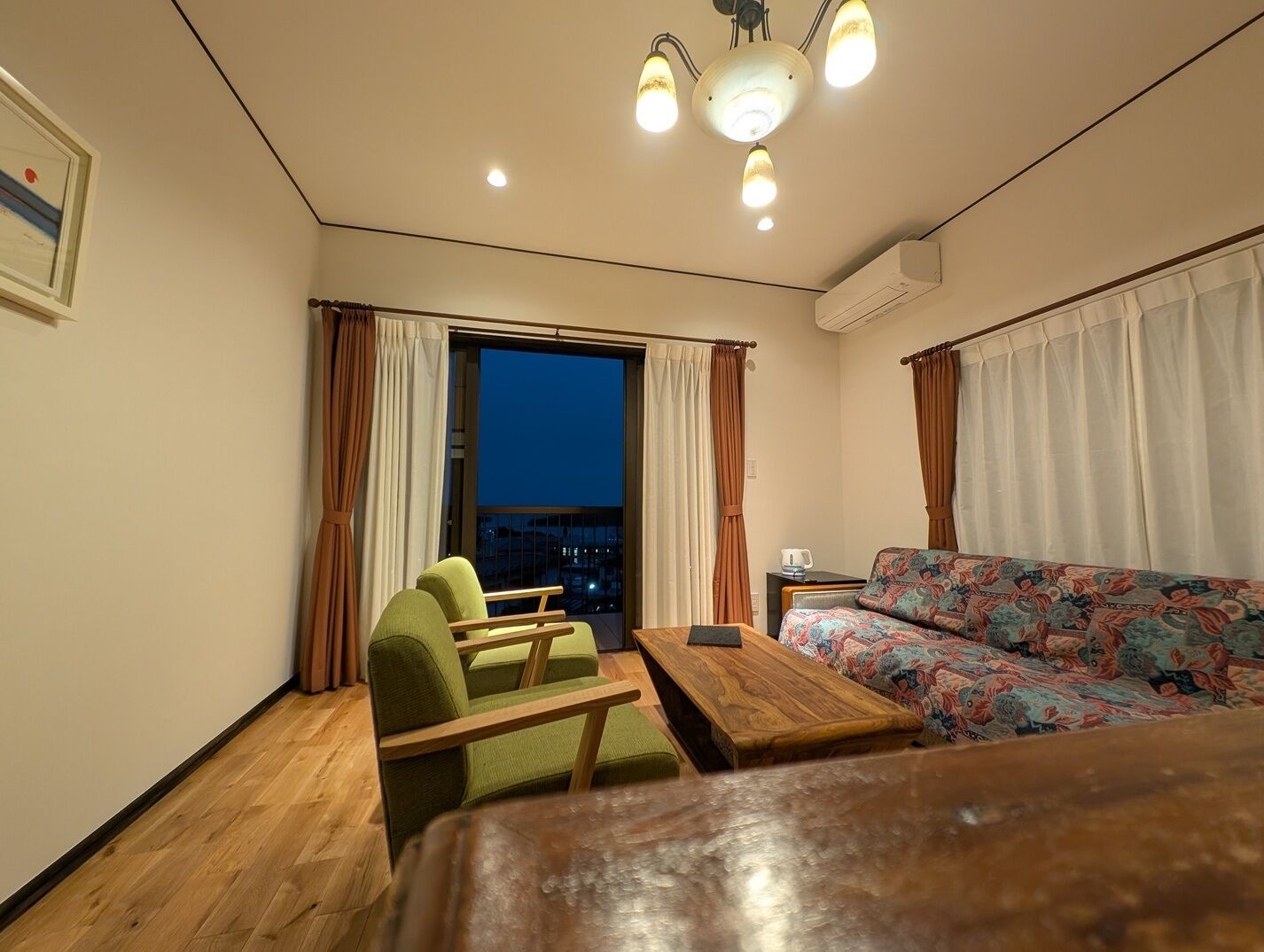 A compact room with a sofa, a chair, a small table, and a window with curtains.