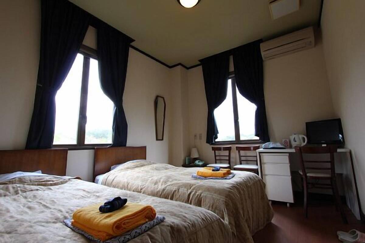 Une chambre d’hôtel avec deux lits, un bureau, une chaise et une télévision.