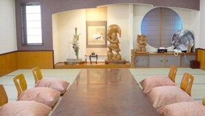 Een vergaderzaal met een lange tafel, stoelen en decoratieve elementen, waaronder sculpturen en een groot rond raam.