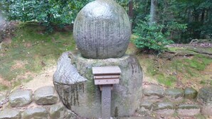 Een stenen monument met een gebeeldhouwde inscriptie, omringd door mosgroene rotsen en begroeiing.
