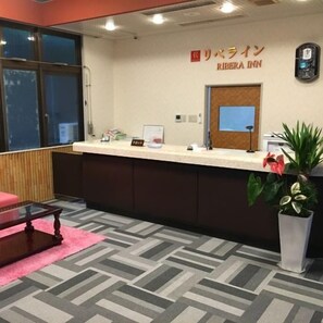 A hotel reception area with a reception desk, a clock, and a potted plant.