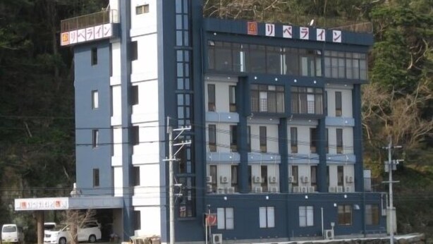 Ein mehrgeschossiges Gebäude mit flachem Dach, vermutlich ein Hotel oder Bürogebäude, mit einer steinernen Basis und von Bäumen umgeben.