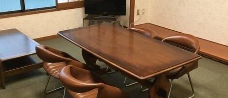 Ein Konferenzraum mit einem Holztisch, sechs Stühlen, einem Fernseher und einer Schiebetür.