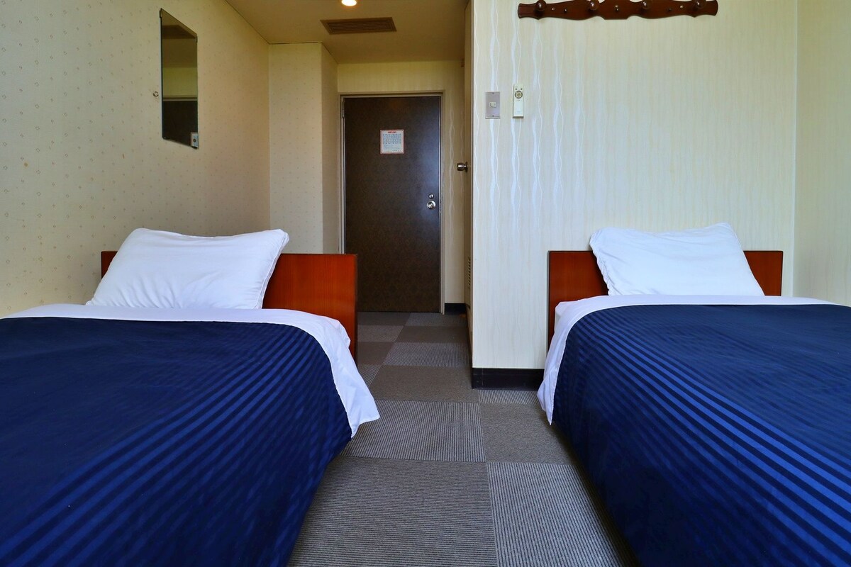 A hotel room with two beds, a door, and a small mirror on the wall.