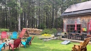 Eine rustikale Holzhütte mit einer Veranda, umgeben von einer grünen Wiese und hohen Bäumen.