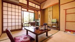 Una habitación tradicional japonesa con suelo de tatami, una mesa baja con un set de té, una silla y un televisor sobre un mueble.