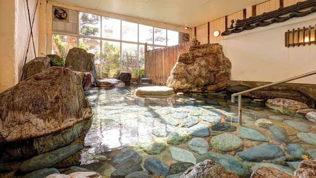 Una piscina de aguas termales de piedra con rocas grandes, una terraza de madera y vistas al exterior.