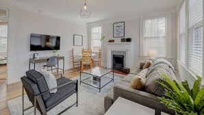 Ein modernes Wohnzimmer mit Sofa, Couchtisch, Fernseher, Kamin und einem Essbereich mit Stühlen.