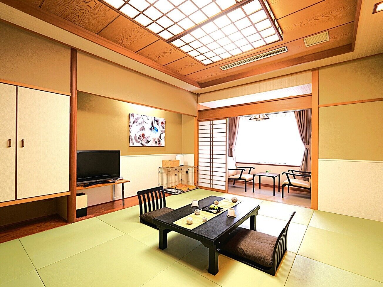 Habitació japonesa tradicional amb tatami, una taula baixa amb coixins, televisió i portes corredisses cap a un balcó.