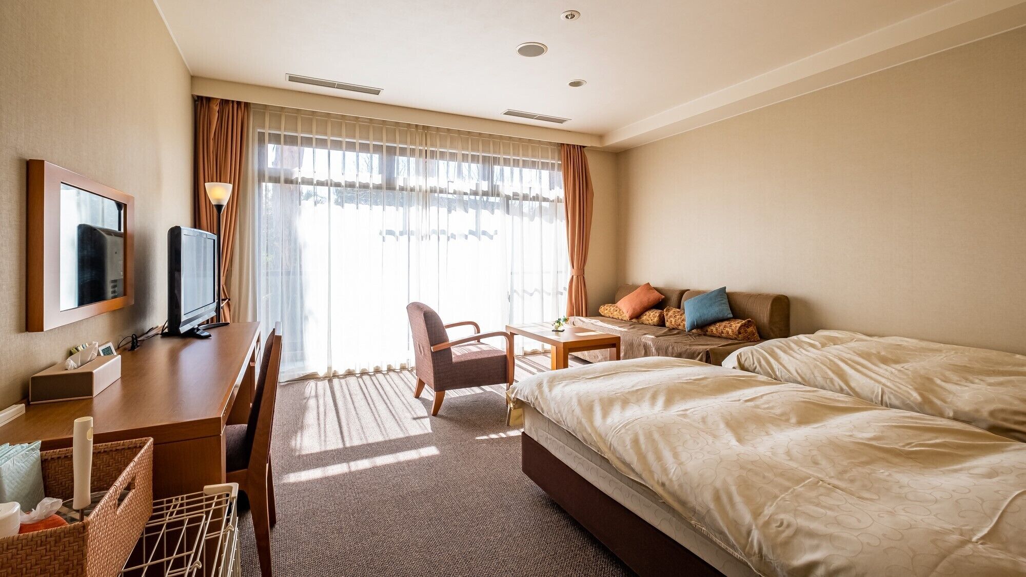 Habitació d'hotel amb un llit, una escriptori amb un ordinador, una cadira, un televisor i una finestra amb cortines.