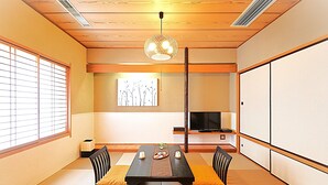Una habitación tradicional japonesa con suelo de tatami, una mesa baja con cojines, un televisor sobre un mueble y puertas correderas.