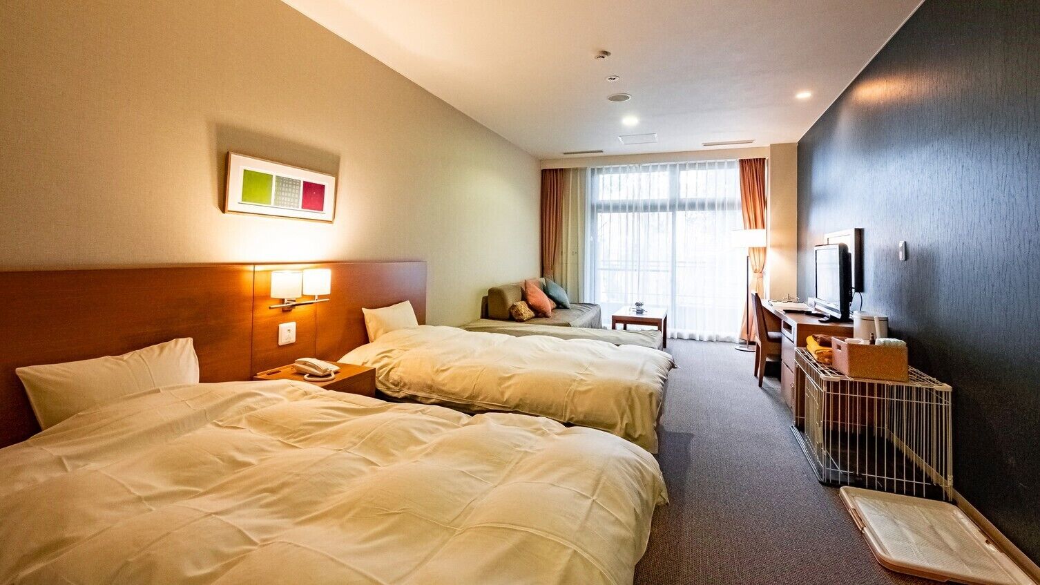 Habitació d'hotel amb dos llits, una taula de treball, un televisor i una finestra amb cortines.